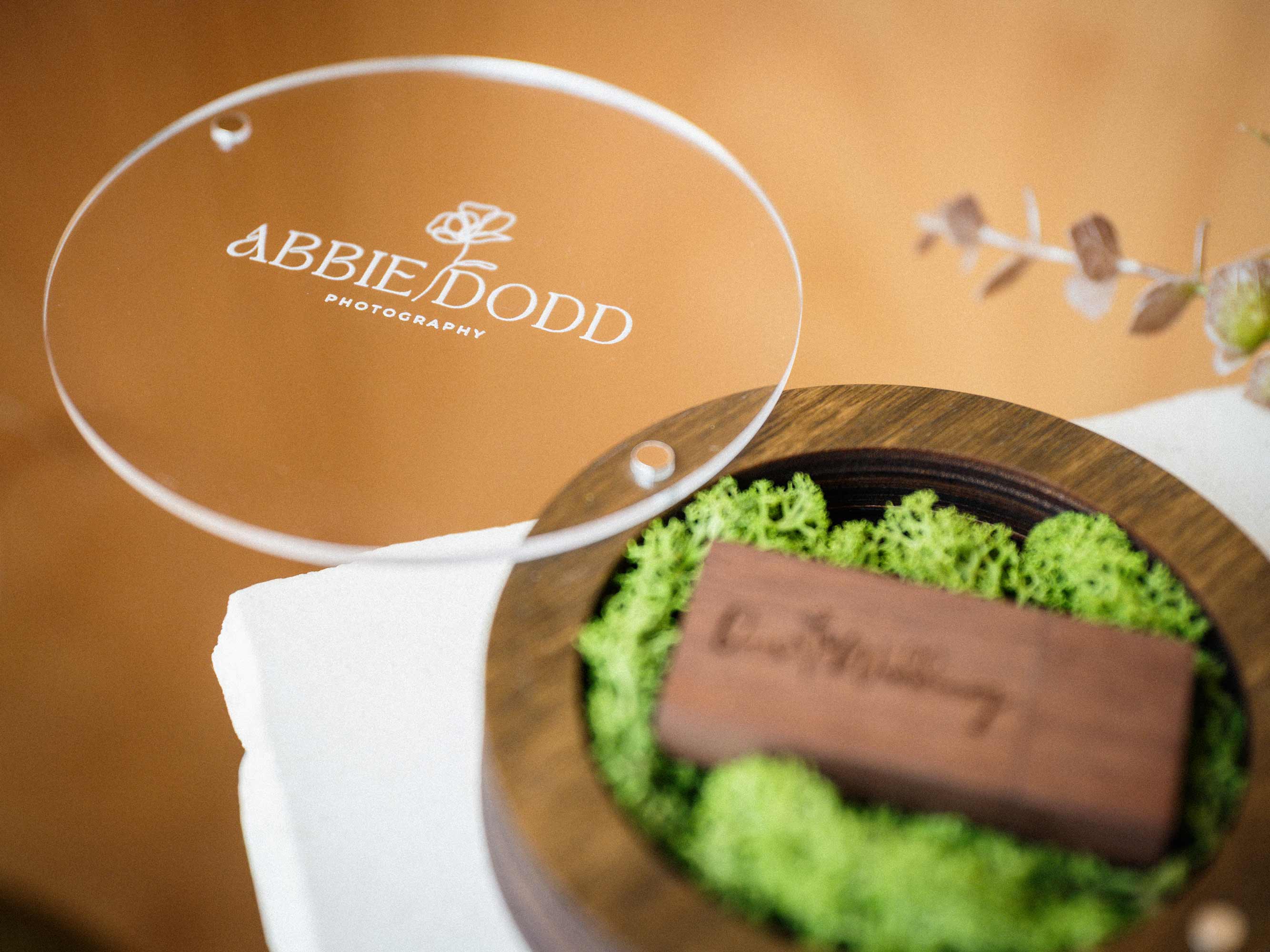 Open walnut USB box with acrylic lid and engraved wooden flash drive on preserved green moss