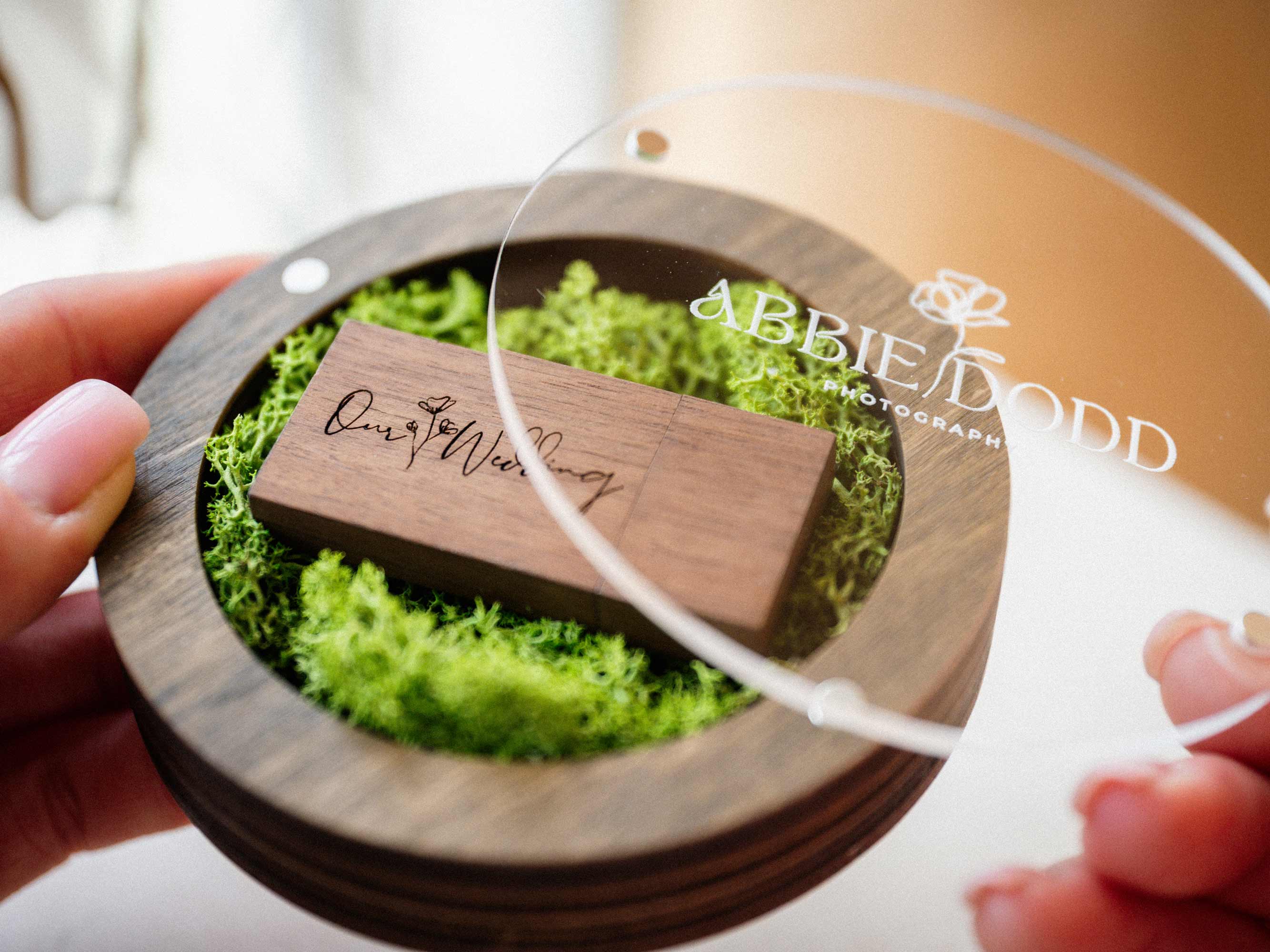 Personalized walnut USB box with acrylic lid, green moss, and wooden flash drive in hands