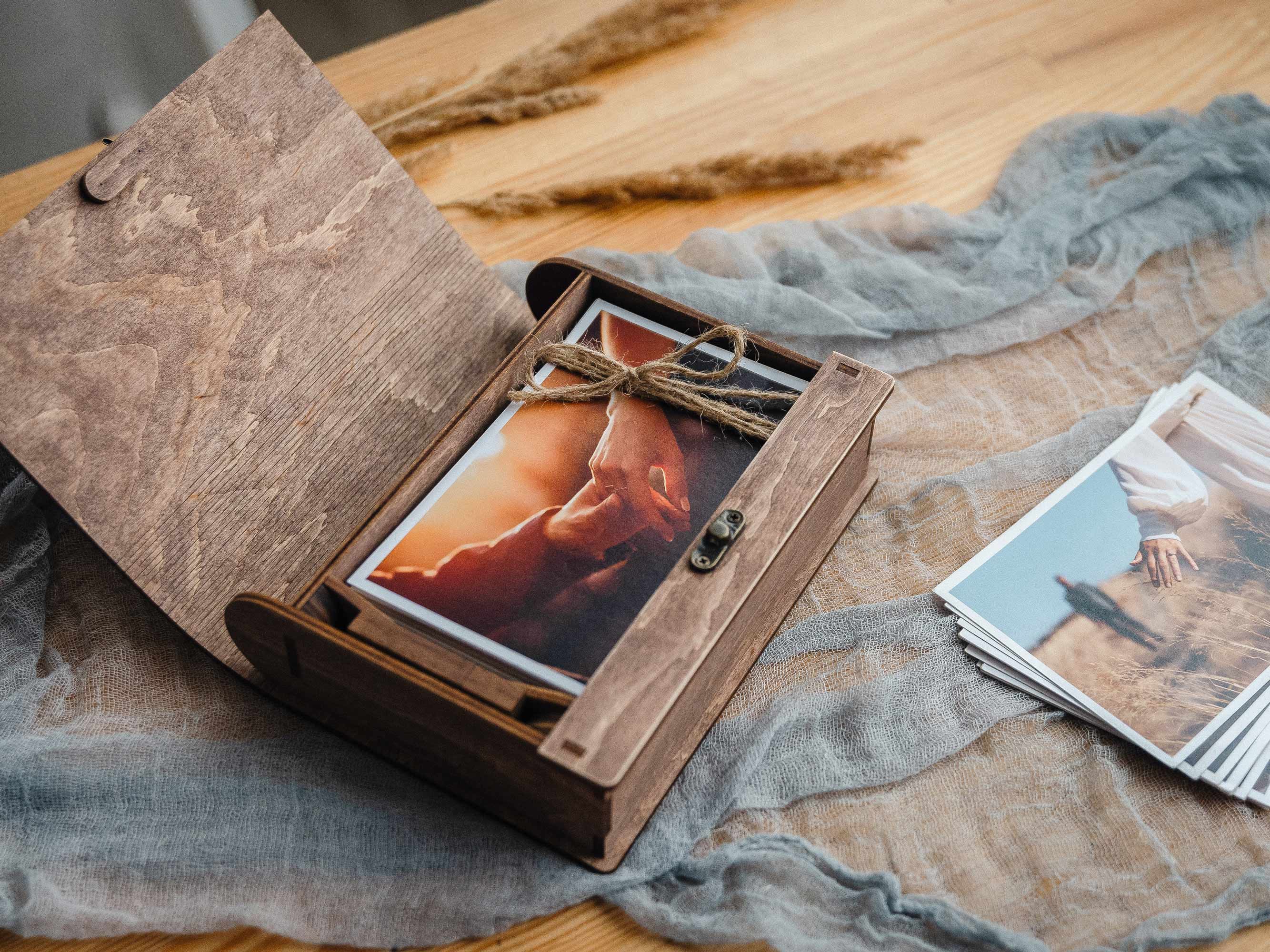 Open walnut photo box on linen with photo prints inside and wooden USB nearby