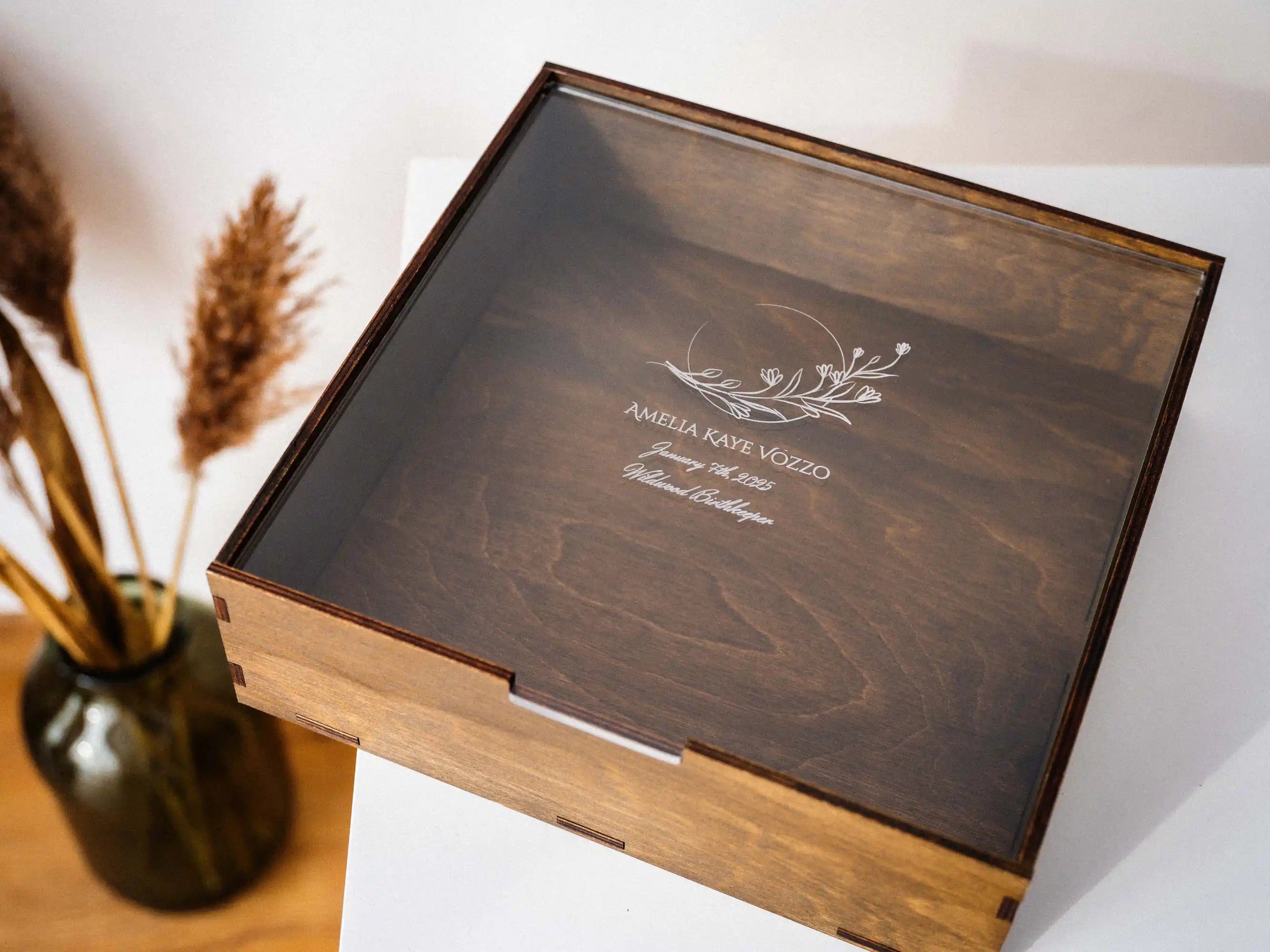 Closed walnut wedding album box with personalized acrylic lid on white table