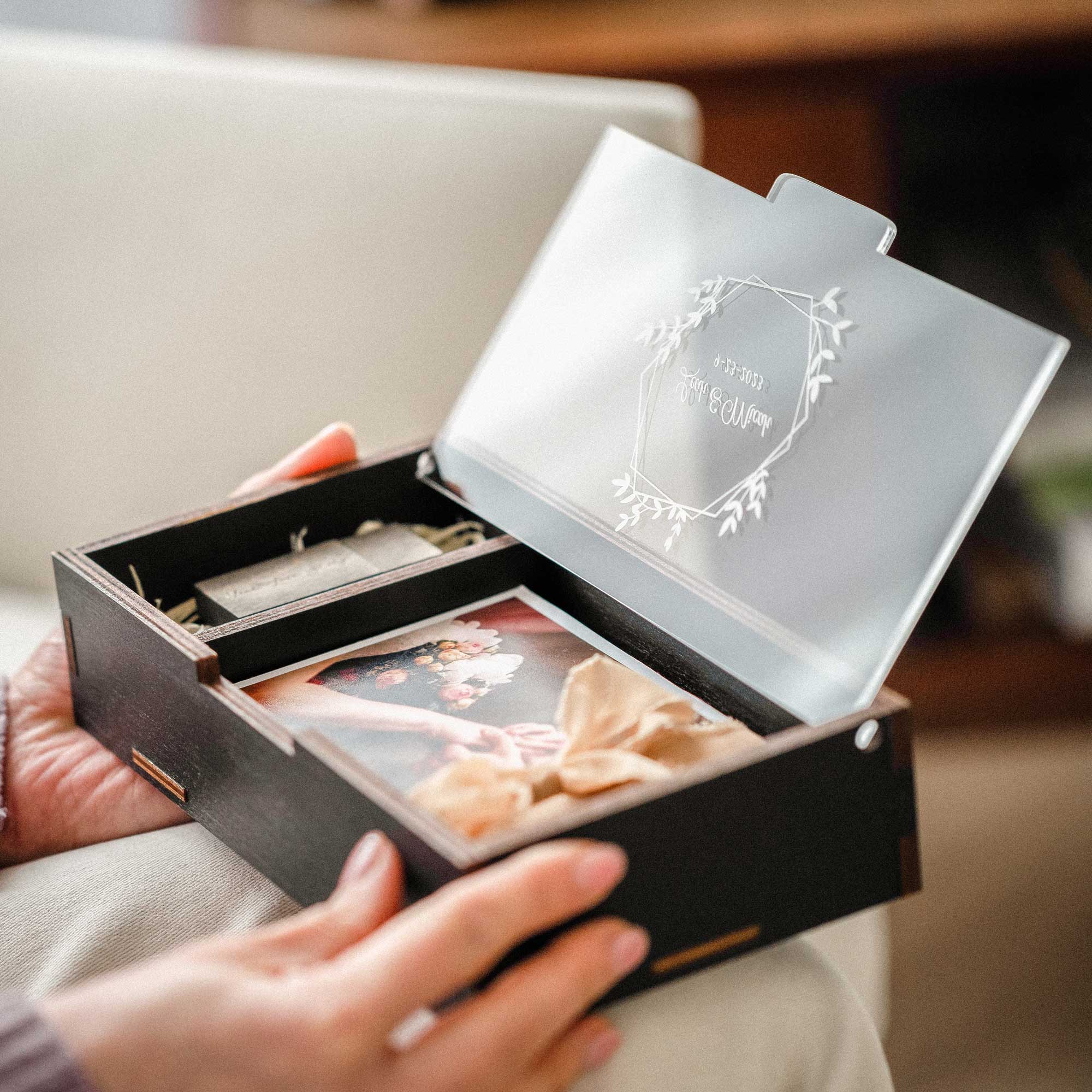 Open black photo box with USB compartment and personalized acrylic lid in hands
