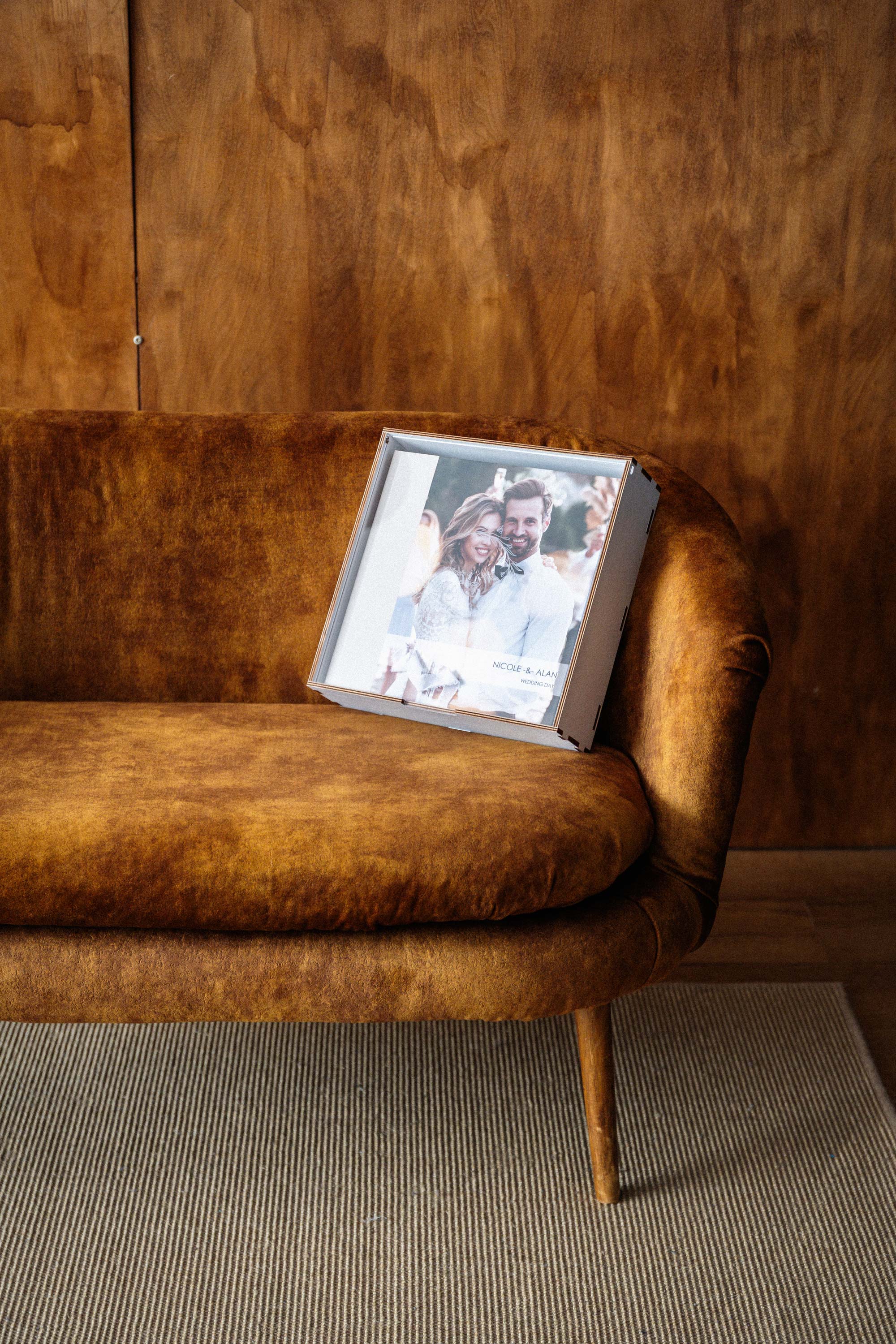 White wooden photo album box for 10x10 album displayed closed on brown sofa