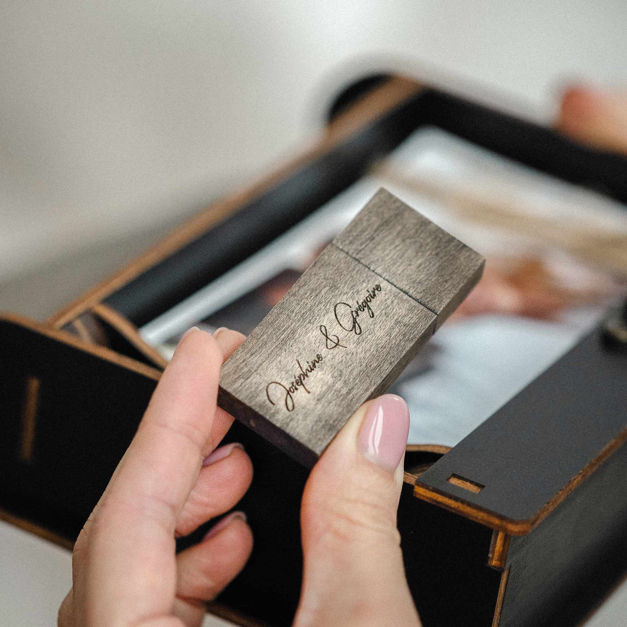 Hands holding engraved wooden USB drive above open photo box, all-in-one wedding keepsake set
