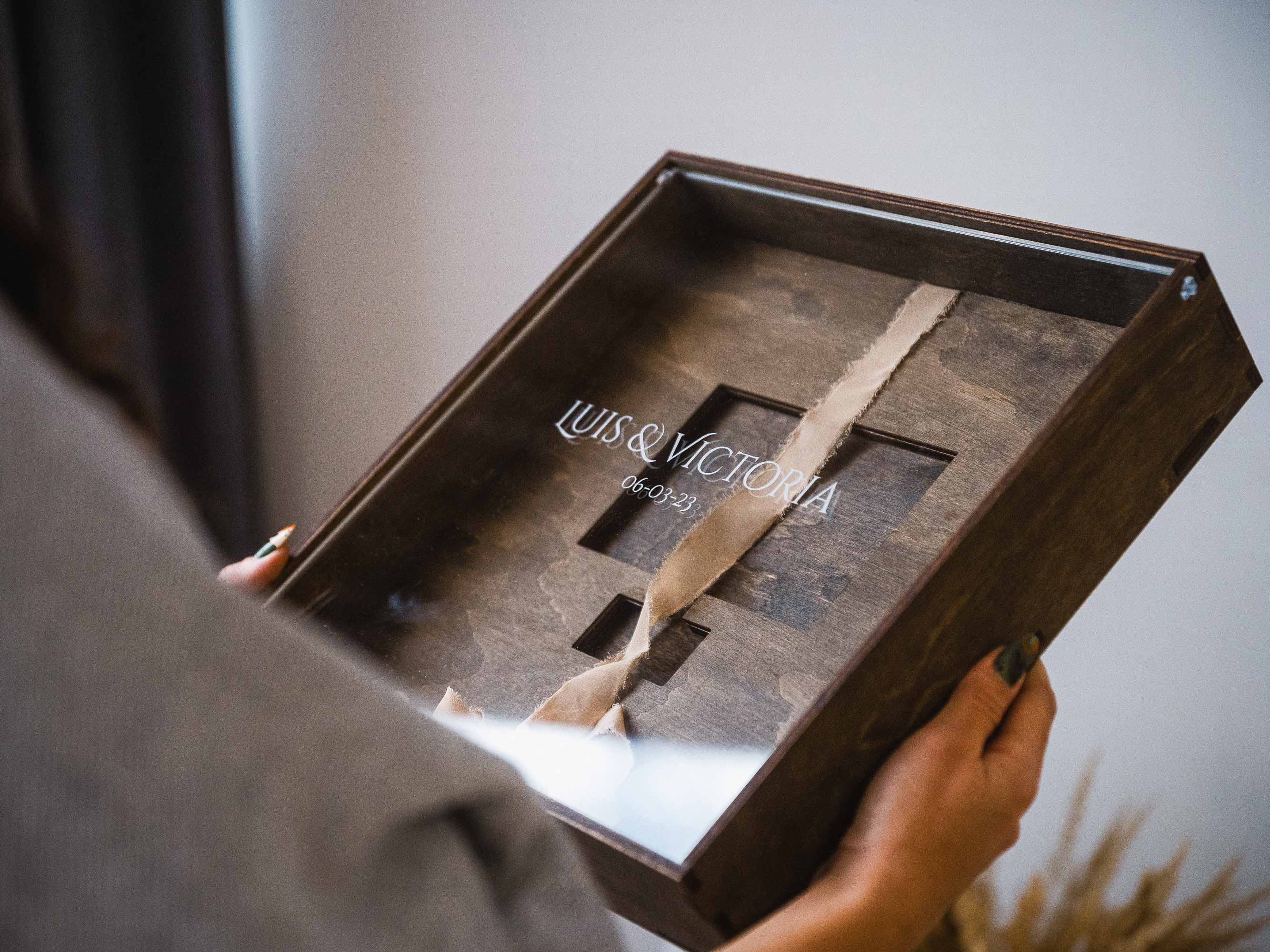 Person holding wooden wedding album box with acrylic lid in hands near window