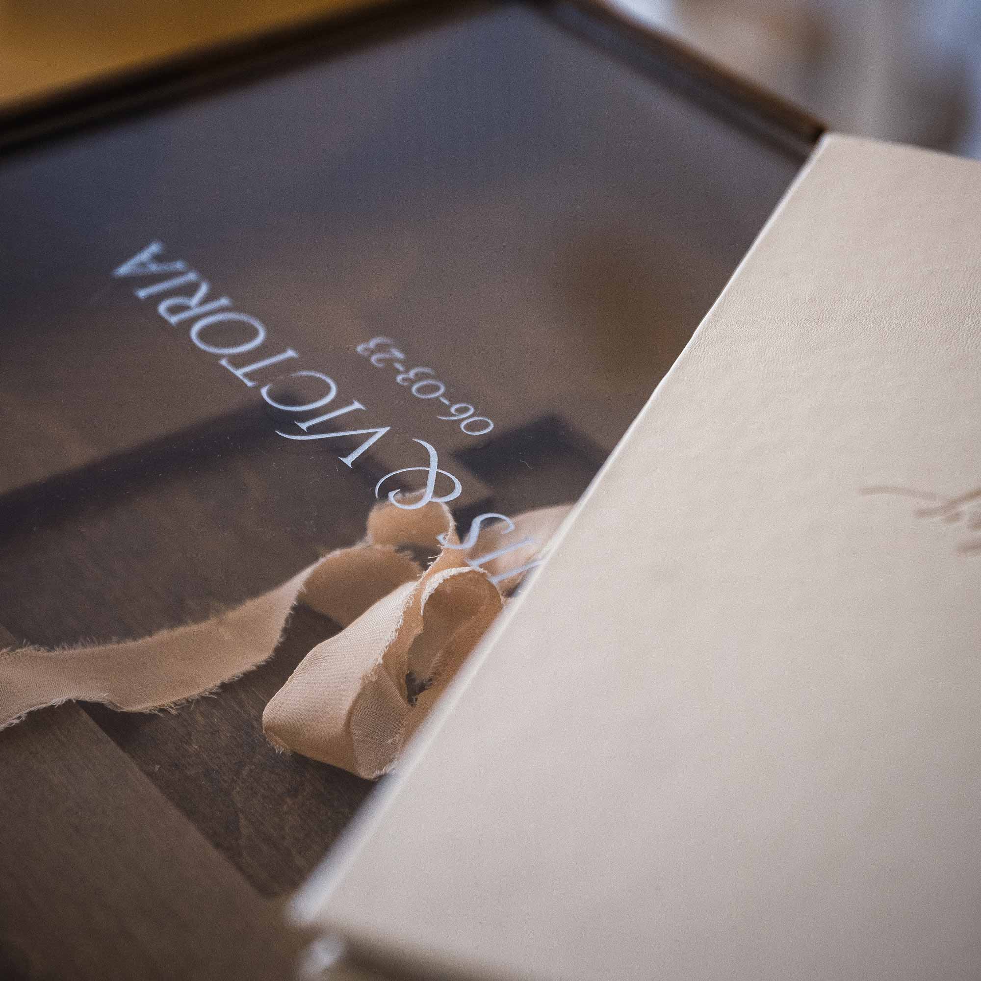 Side view of wooden wedding album box with acrylic lid and silk ribbon inside