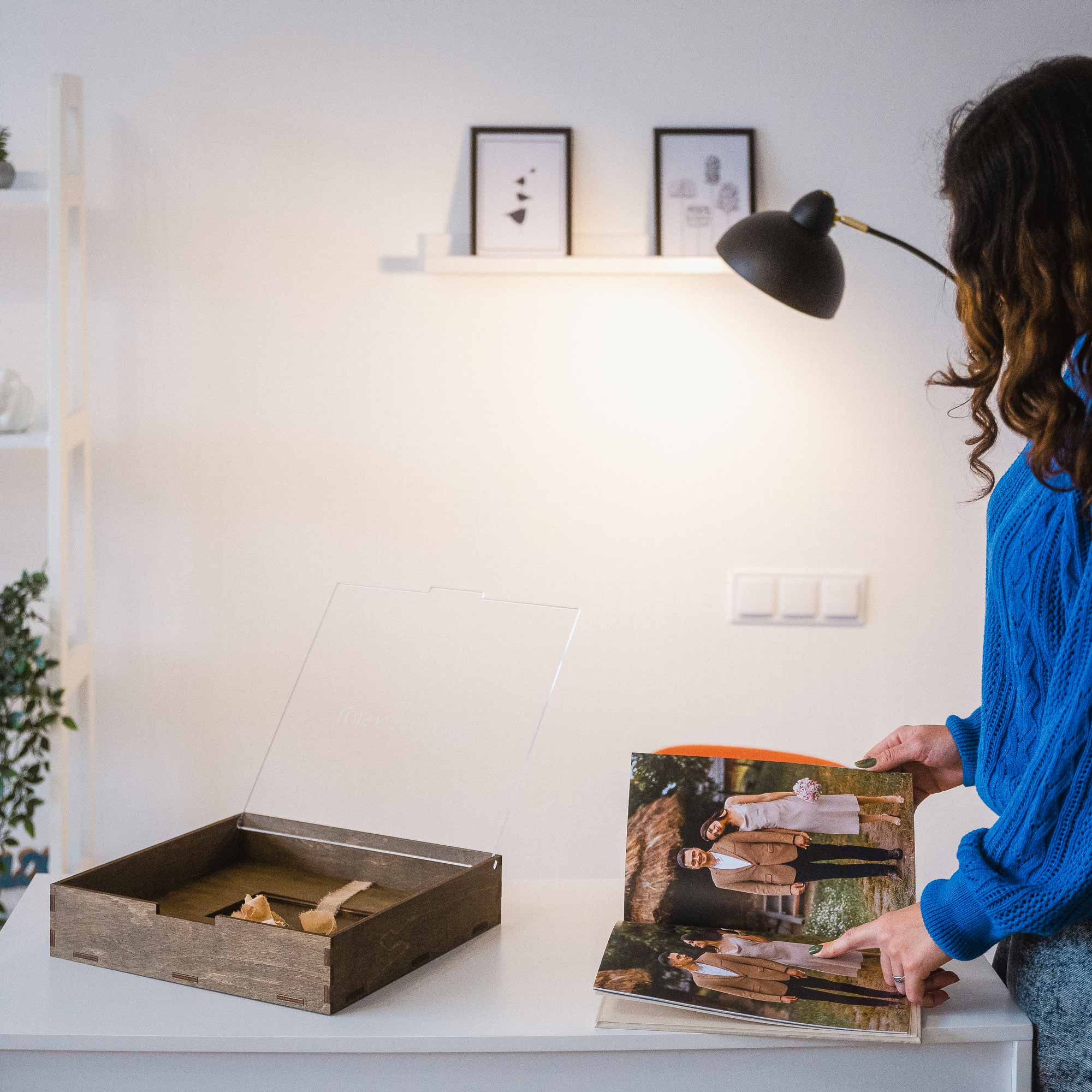 Photographer in blue sweater presenting wooden wedding album box and photo album on shelf